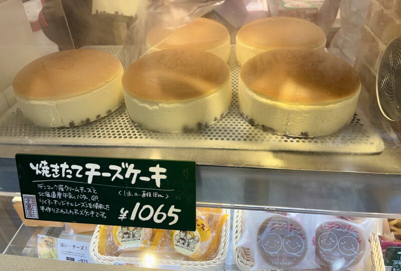 りくろーおじさんの店の焼きたてチーズケーキが並ぶショーケースと、価格表示「焼きたてチーズケーキ 1065円」の看板