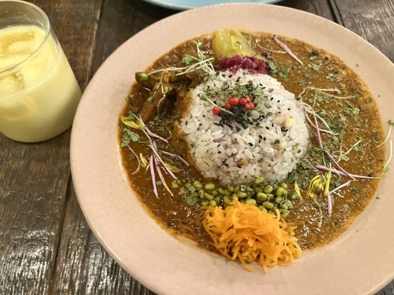 スパイスカレー（カレーの惑星）の一皿。雑穀ごはんと副菜が添えられ、横にドリンクが置かれている写真。